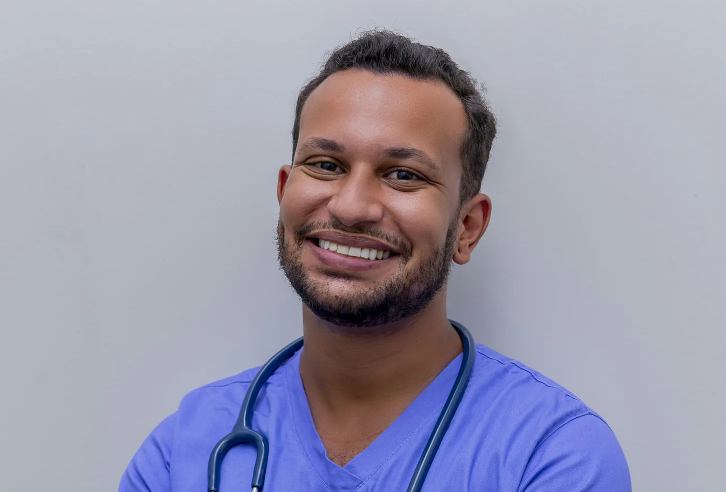 Smiling clinician in blue scrubs with a stethoscope